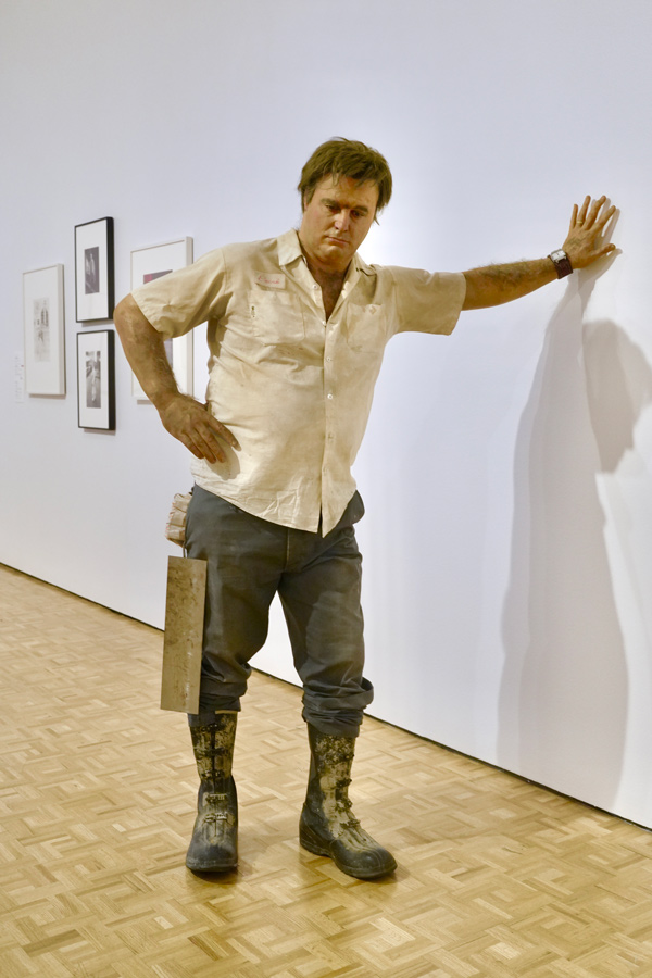 a hyper realistic sculpture of a man resting his hand on the wall