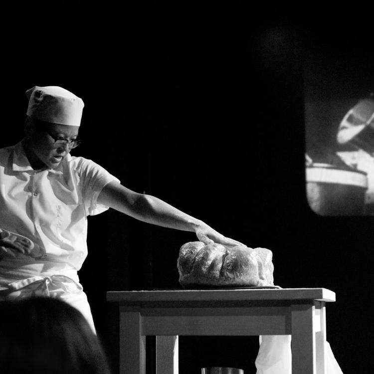 A black and white image of a man standing by a table
