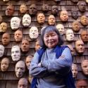 An image of artist Ruth Asawa infront of her Wall of Masks