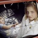 An image of a girl and a baby inside a red car