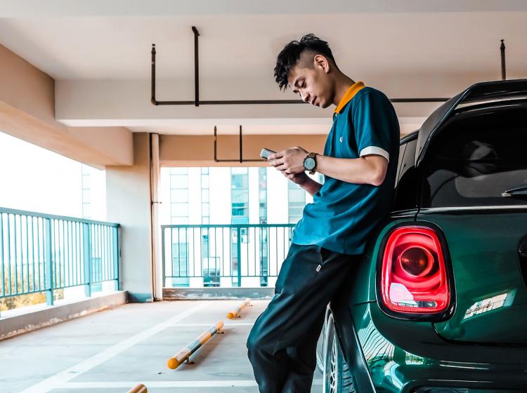 A man using his phone and leaning on his car