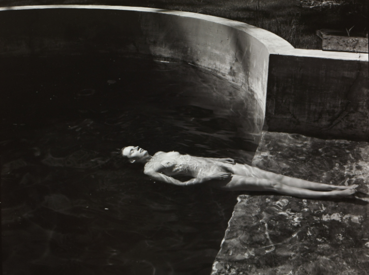 A black and white image of a naked woman floating in a pool