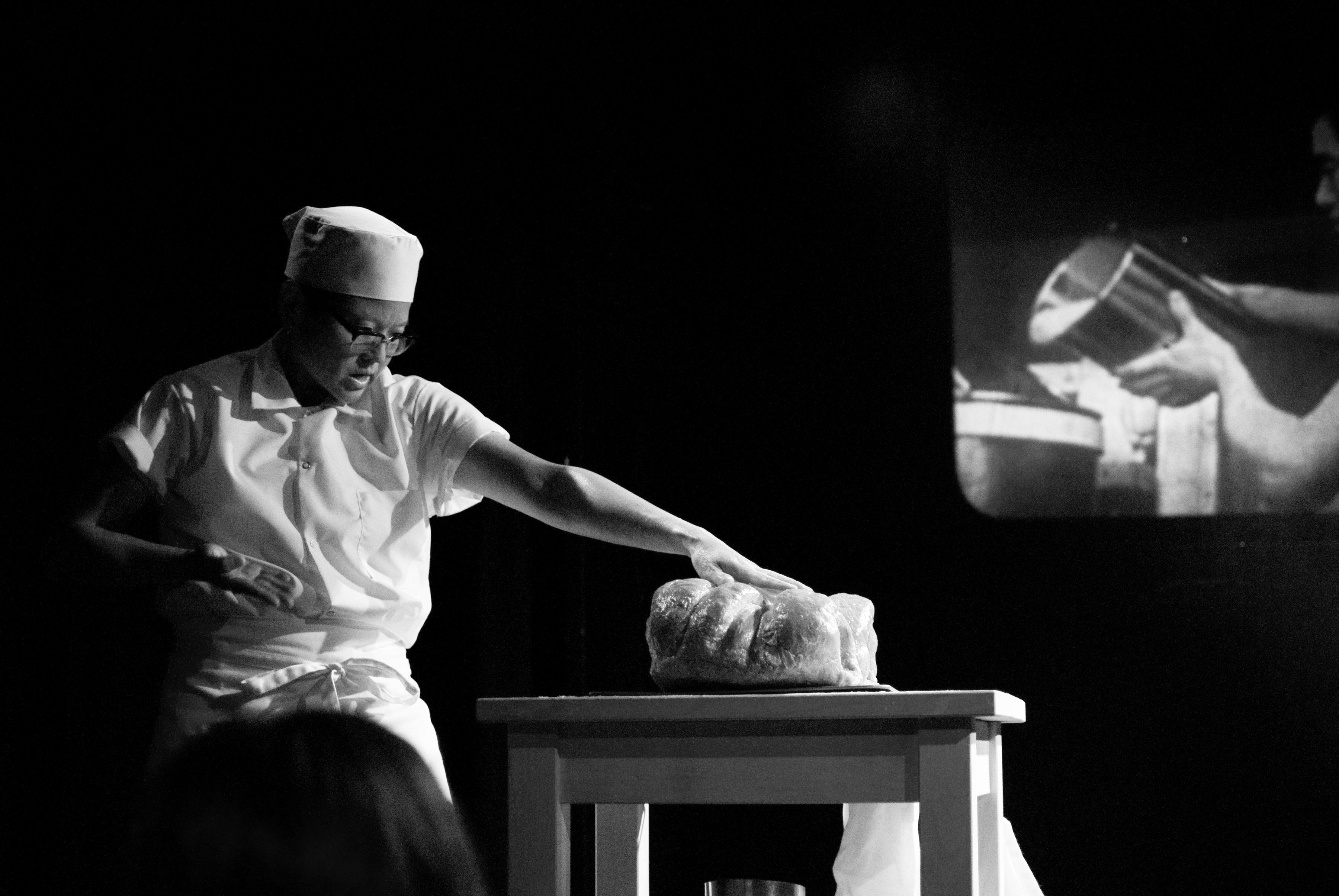 A black and white image of a man standing by a table