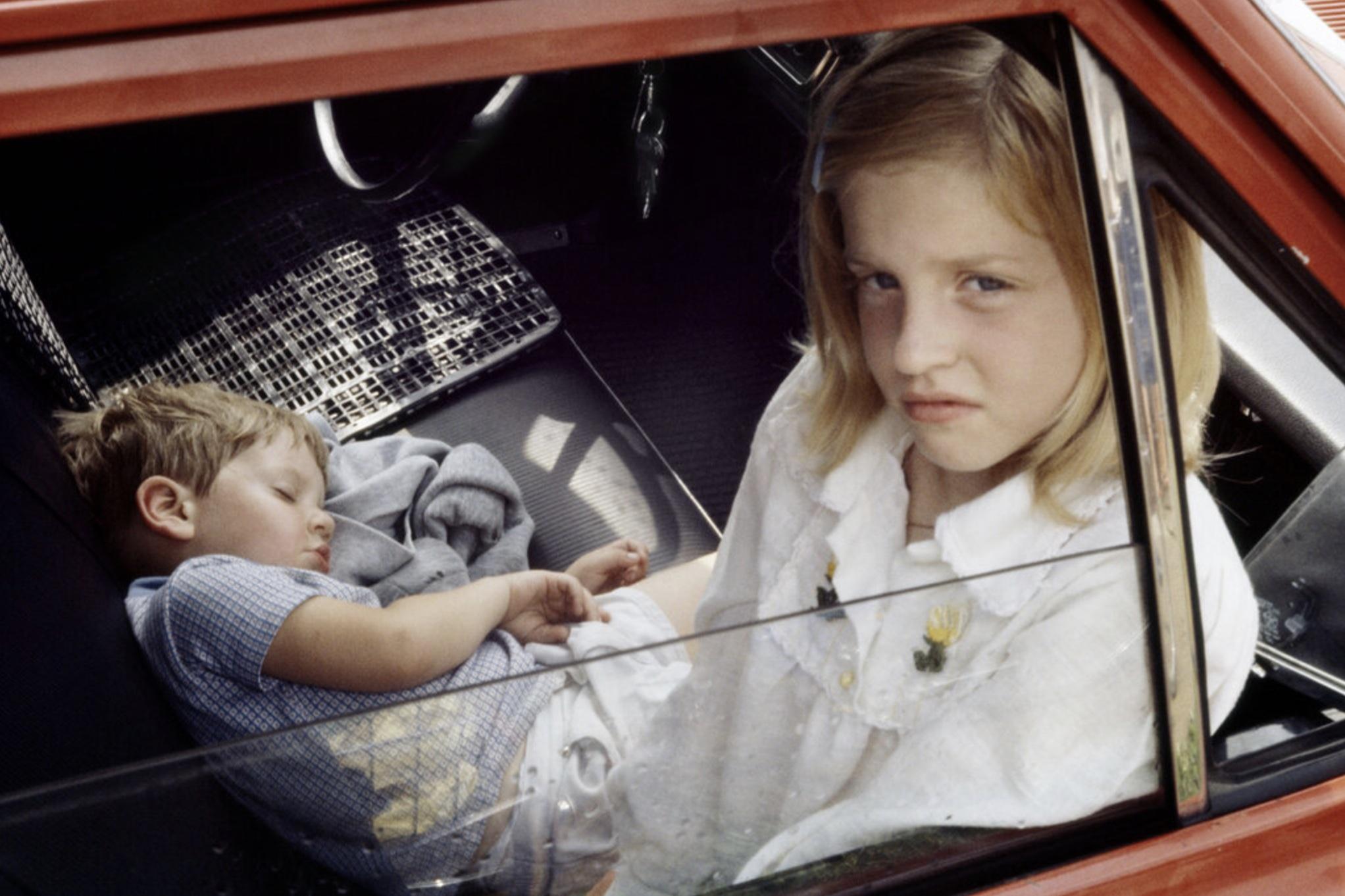 An image of a girl and a baby inside a red car